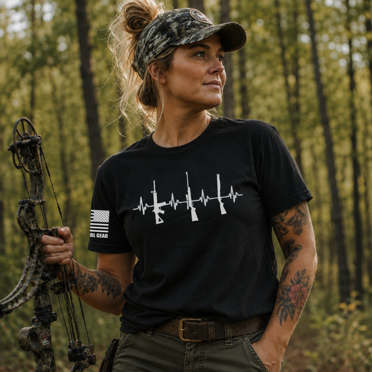 A woman in a forest setting wearing a black t-shirt with a white rifle heartbeat graphic and 'AR MIGHT GEAR' on the sleeve, holding a compound bow.