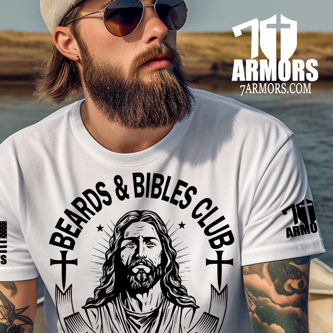 A man wearing a white graphic t-shirt with a black print of Jesus Christ and the text 'Beards & Bibles Club'. The background shows a blurred outdoor beach scene.