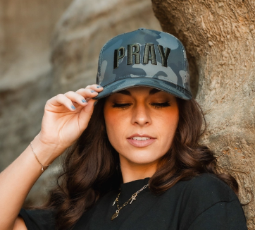 Person wearing a cap with 'PRAY' on it against a natural background