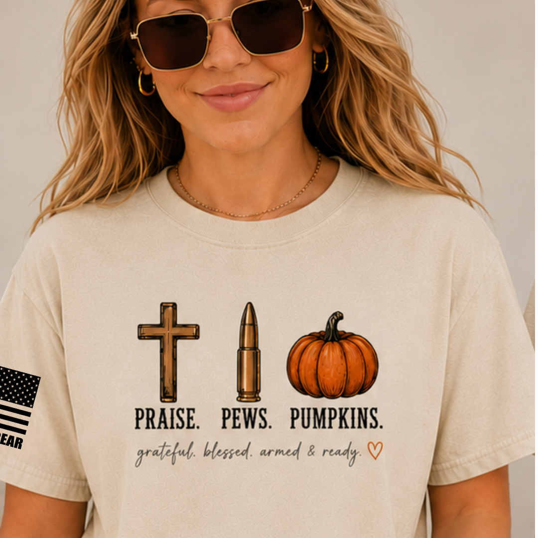 A woman wearing a beige graphic t-shirt with a cross, bullet, and pumpkin design with the text 'PRAISE. PEWS.