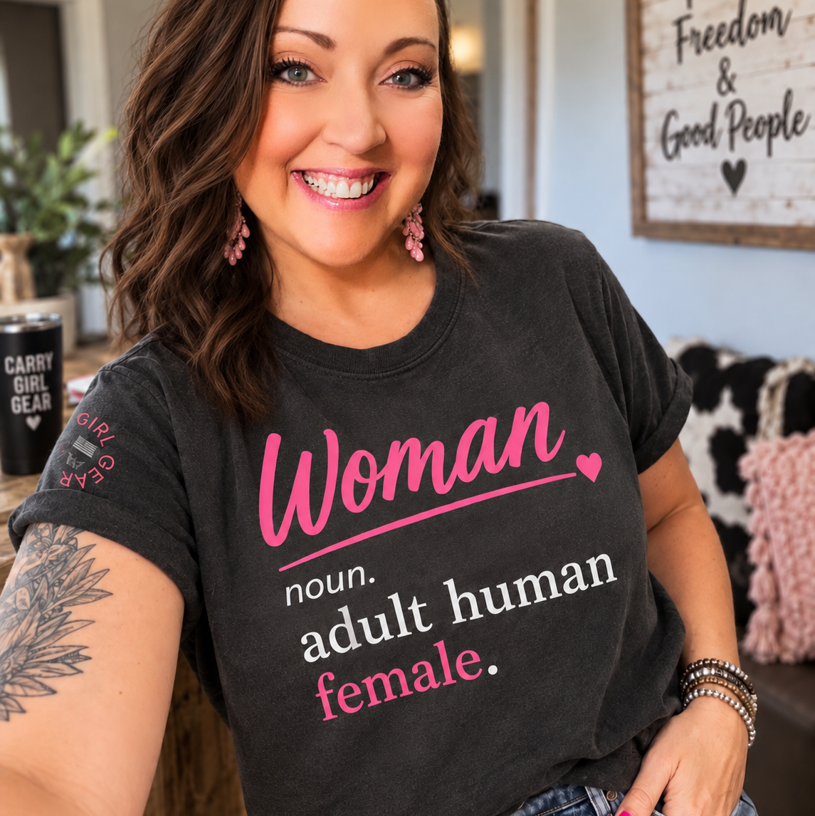 A smiling woman wearing a black graphic t-shirt with pink and white text that reads 'Woman noun. adult human female.